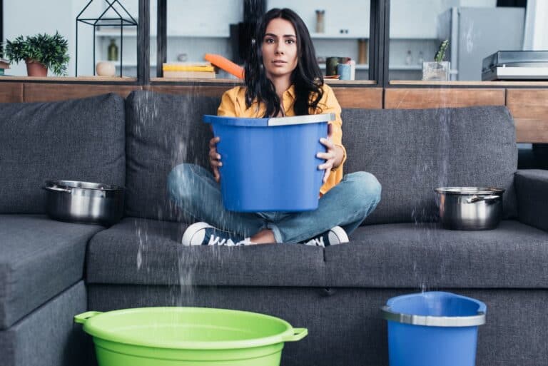 woman using buckets to catch water from roof leak during heavy rain