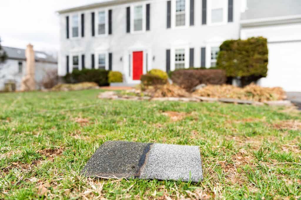 Front yard of house during day aftermath after storm roof tile shingle lying down on grass, damage closeup