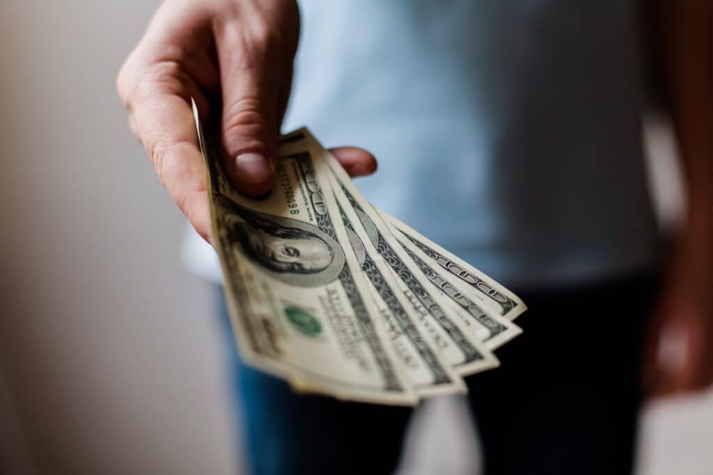 man paying cash out of pocket - holding hundred dollar bills