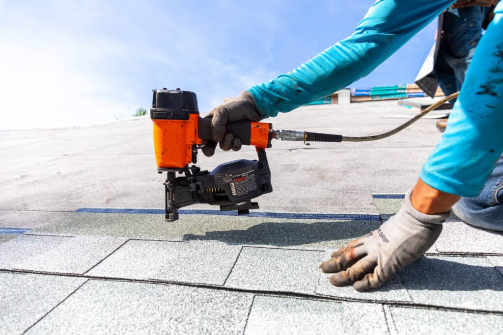 roofer installing roof shingles with pnuematic roofing nailer.